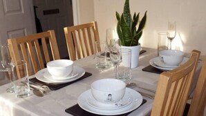 Een eettafel gedekt met witte borden, kommen en bestek, inclusief glazen en een bloempot met plant.