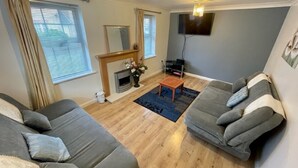 Een woonkamer met twee grijze banken, een houten salontafel, een open haard en een flatscreen televisie aan de muur.