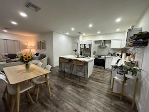 Une cuisine moderne dotée d’un îlot central, de meubles blancs et d’un coin repas avec une table et des chaises en bois.