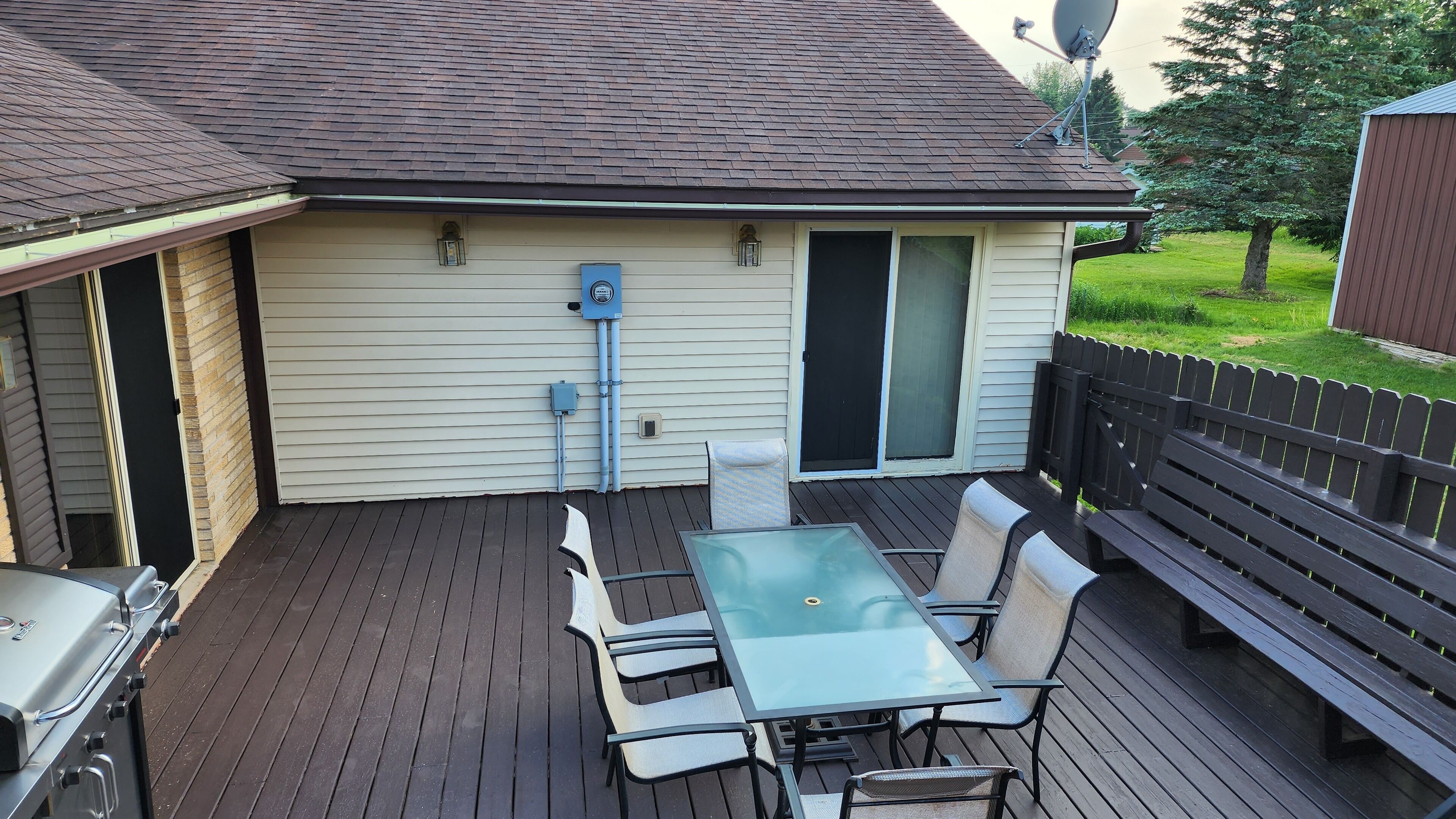 A deck with a glass-top table and chairs, a barbecue grill, and a covered patio area.