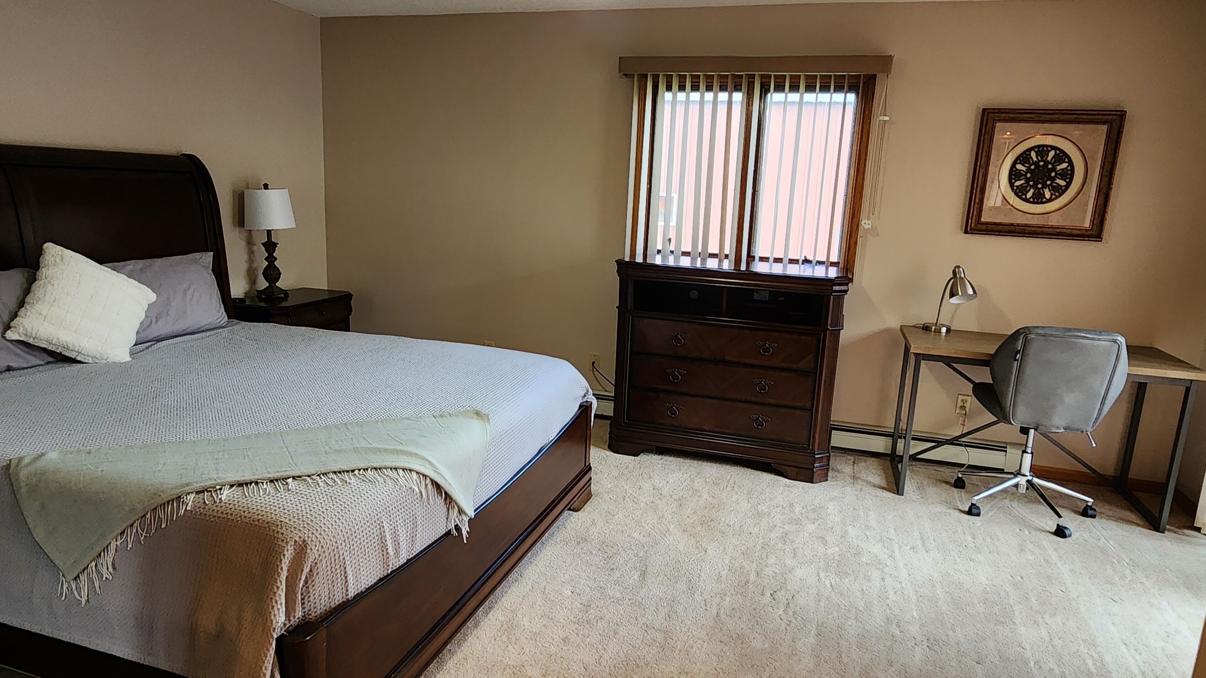 A bedroom with a bed, dresser, desk, chair, and a framed picture on the wall.