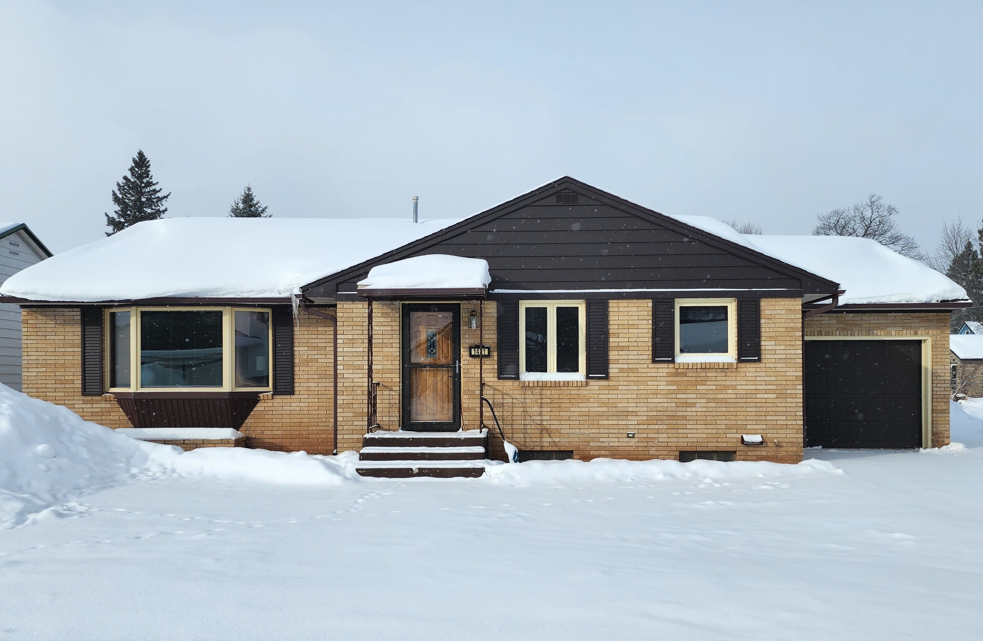 Une maison à deux étages, dont le toit est recouvert de neige et les murs sont en briques.