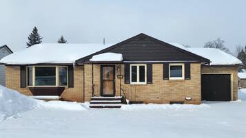 Une maison à deux étages, dont le toit est recouvert de neige et les murs sont en briques.