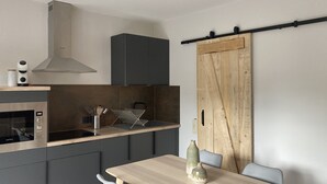 Eine moderne Küche mit Einbauofen, Mikrowelle und Edelstahl-Dunstabzugshaube. Ein Holztisch mit zwei Stühlen und einer Vase steht daneben.