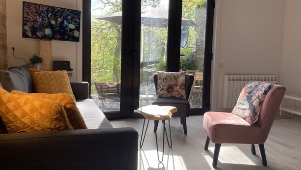 Ein Wohnzimmer mit einer Couch, Sesseln und einem Couchtisch. Ein großes Fenster bietet einen Ausblick ins Freie.