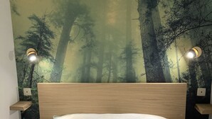 Ein Schlafzimmer mit einem Bett, einem Kopfteil, einem Wandgemälde von einem Wald und zwei Nachttischlampen.
