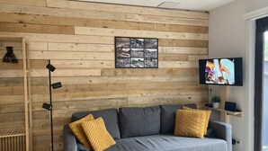 Ein modernes Wohnzimmer mit grauem Sofa, Holzpaneelen, einer schwarzen Stehlampe, einem gerahmten Schwarz-Weiß-Foto und einem Fernseher auf einem Holzboden.