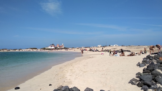 Een strand met heldere lucht, een zandstrand en een gebouw met een rood dak op de achtergrond.