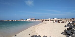 A beach with clear skies, a sandy shore, and a building with a red roof in the background.