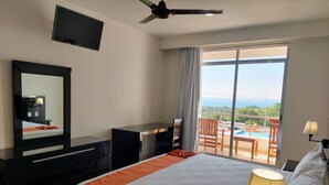 Une chambre d’hôtel comprenant un lit, un bureau, une chaise, une télévision et un balcon avec vue sur l’océan.