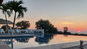 Une piscine avec des chaises longues, des palmiers et une vue imprenable sur le coucher de soleil.