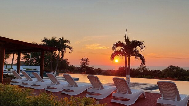 Un espace aménagé au bord de la piscine, avec des chaises longues et une vue sur le coucher de soleil.