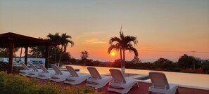 Uma área à beira da piscina com espreguiçadeiras e vista para o pôr do sol.