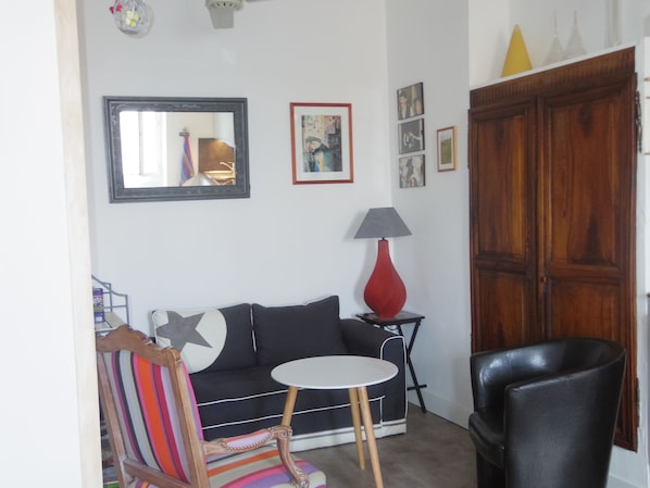 A living room with a sofa, a striped chair, a small round table, a lamp, and a wooden cabinet.