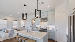 A modern kitchen with a central island, white cabinetry, stainless steel appliances, and wooden stools.