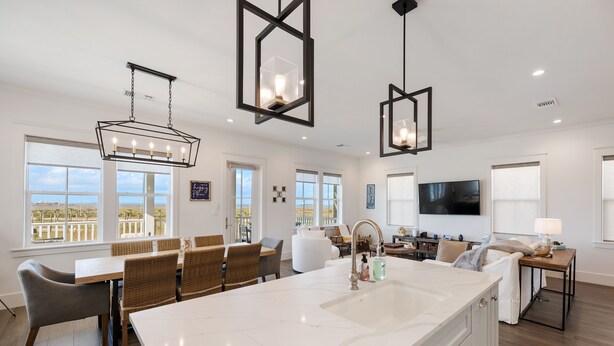 A spacious kitchen with a large island, modern pendant lights, and a view of the outdoors through large windows.