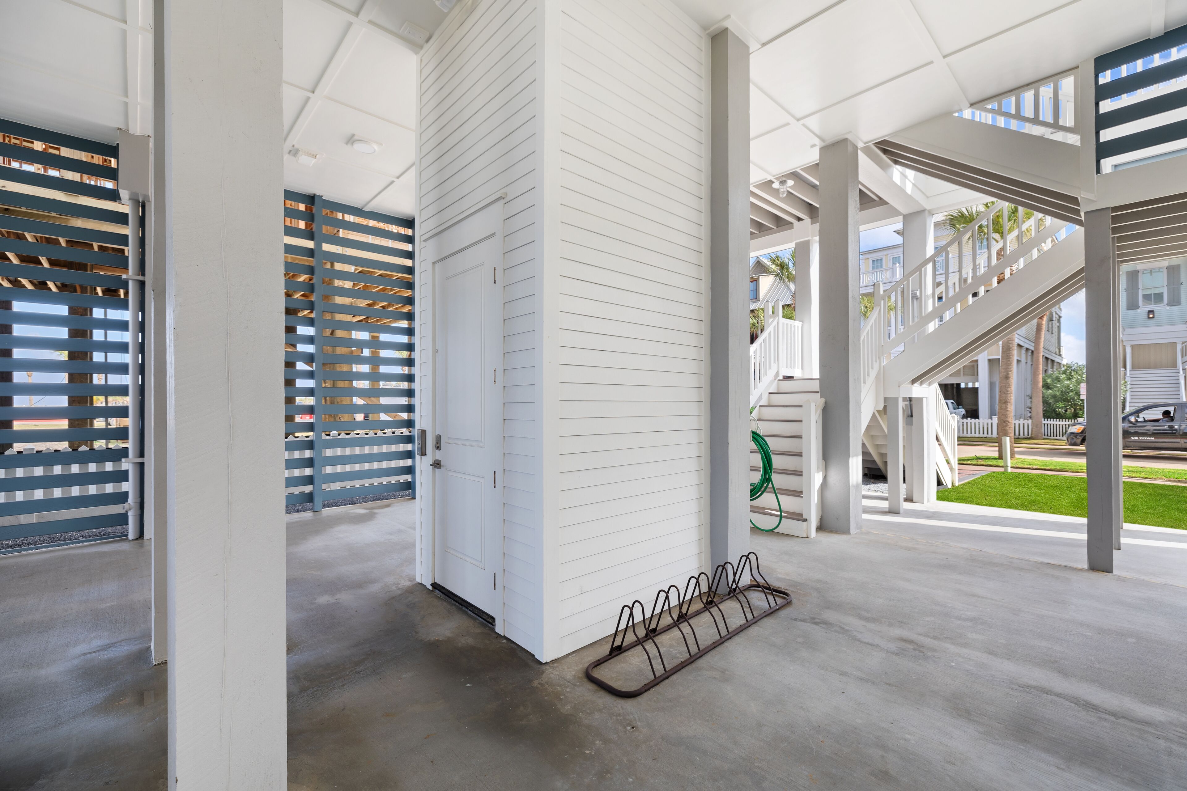 A spacious covered area with a concrete floor, a metal bike rack, and a white building with horizontal siding.