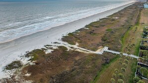 An aerial view of a coastal area with a beach, a white bridge, and a row of buildings.