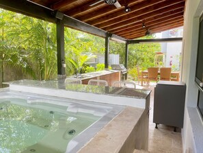 Unwind in a serene outdoor oasis with a hot tub, pergola, and comfortable seating area amidst lush greenery.