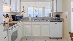 A kitchen with white cabinets, a microwave, a coffee maker, and a view of the sea through large windows. - Oceanfront Paradise: Your Dream Beachfront Escape (Panama City Beach)
