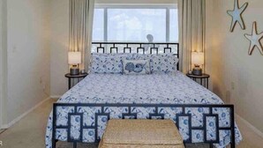 A bedroom with a bed, two bedside tables, a window, and a star-shaped decoration on the wall. - Oceanfront Paradise: Your Dream Beachfront Escape (Panama City Beach)