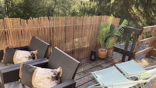 Un patio amueblado con muebles de mimbre, incluyendo un sofá y una silla de relax, y una pequeña mesa con una planta en maceta.