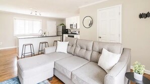 A modern living room with a grey sectional sofa, a small black side table, and a window with blinds.