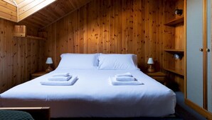 A wooden-paneled room with a bed, two bedside tables, and a lamp on each. - Italianway - Capitano Grandi 5 (Bormio)