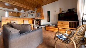 A cozy living room with a sofa, a wicker chair, a fireplace, wooden cabinets, and a television. - Italianway - Capitano Grandi 5 (Bormio)