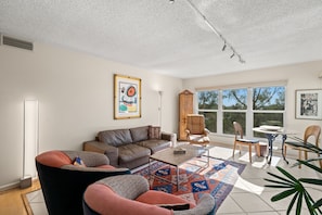 A living room with a sofa, armchairs, a coffee table, and a rug. There are windows, a door, and a painting on the wall. - Long Boat Key Vacation Home (Longboat Key)