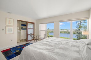 A bedroom with a large bed, a view of a lake, a closet, and a desk with chairs.