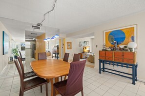 A spacious dining area with a wooden table and chairs, a blue console table with drawers, and a large abstract painting on the wall.