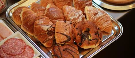 A tray of assorted pastries including croissants and chocolate-topped pastries, alongside a plate of salami and cheese.