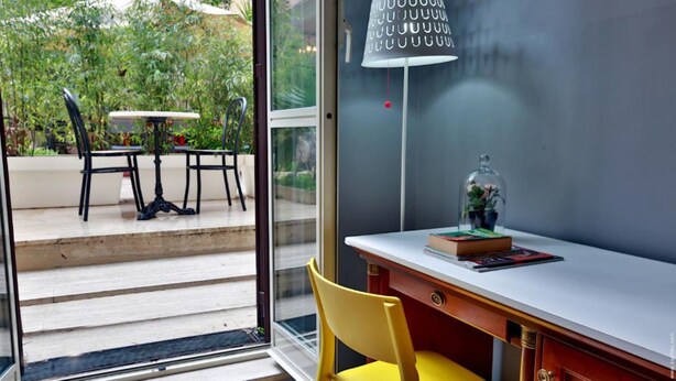 A modern room with a glass door leading to an outdoor area with a table and chairs. Inside, there's a desk with a chair, a lamp, and a book. - Hotel Giolitti Smart (Rome)