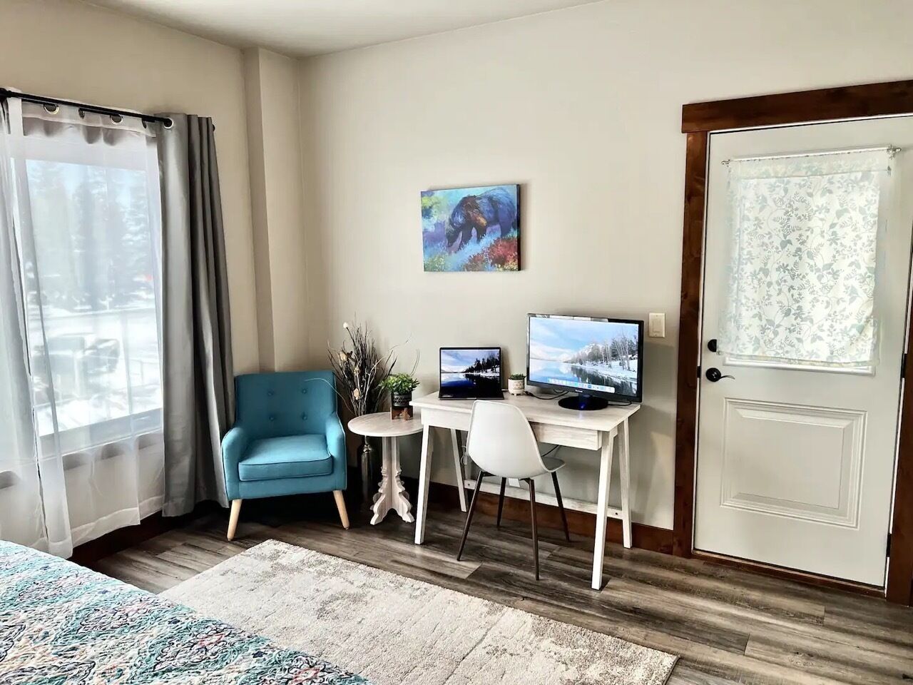 Une chambre d’hôtel avec un lit, un bureau avec un ordinateur, une chaise, une fenêtre avec des rideaux et une porte.