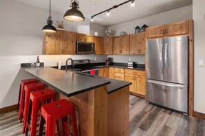 Una cocina moderna con armarios de madera, un refrigerador de acero inoxidable, una isla central con taburetes rojos y una encimera negra.