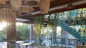 Un café al aire libre con mesas y sillas, plantas colgantes y una escalera azul.