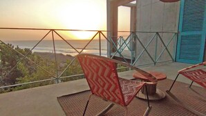 Un balcón con vista al océano al atardecer, con dos sillas de diseño y una mesa.