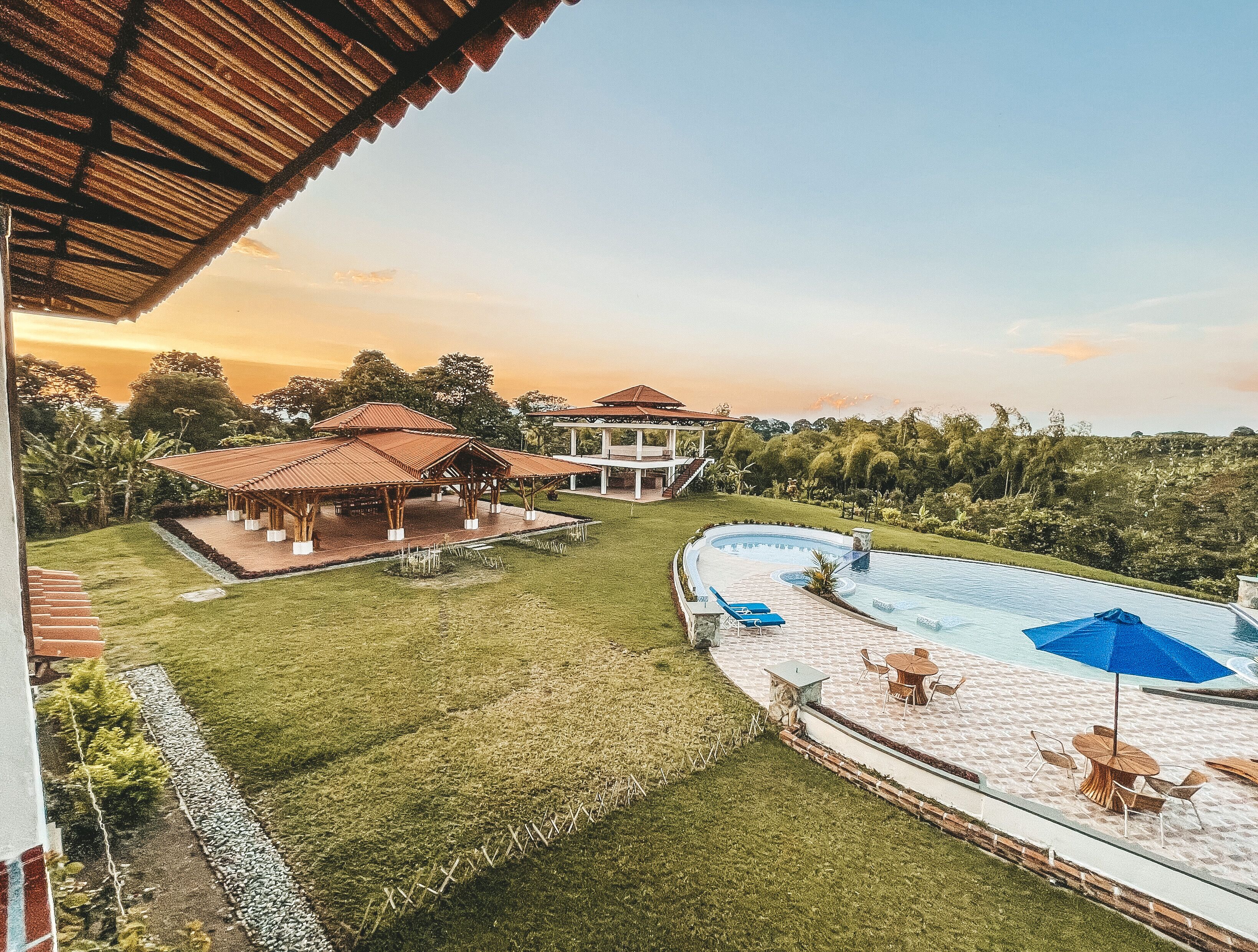 Un resort con piscina, zonas de estar al aire libre cubiertas y abundante vegetación.