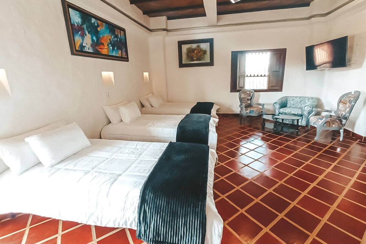 Une chambre d’hôtel avec un grand lit, un lit plus petit, deux chaises, une table et un tableau au mur.