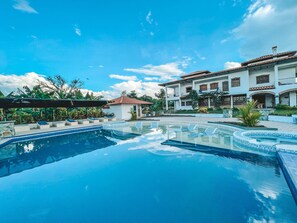 A large swimming pool with a clear blue sky and a multi-story building in the background. - Hotel la Casona Montañesa (Montenegro)