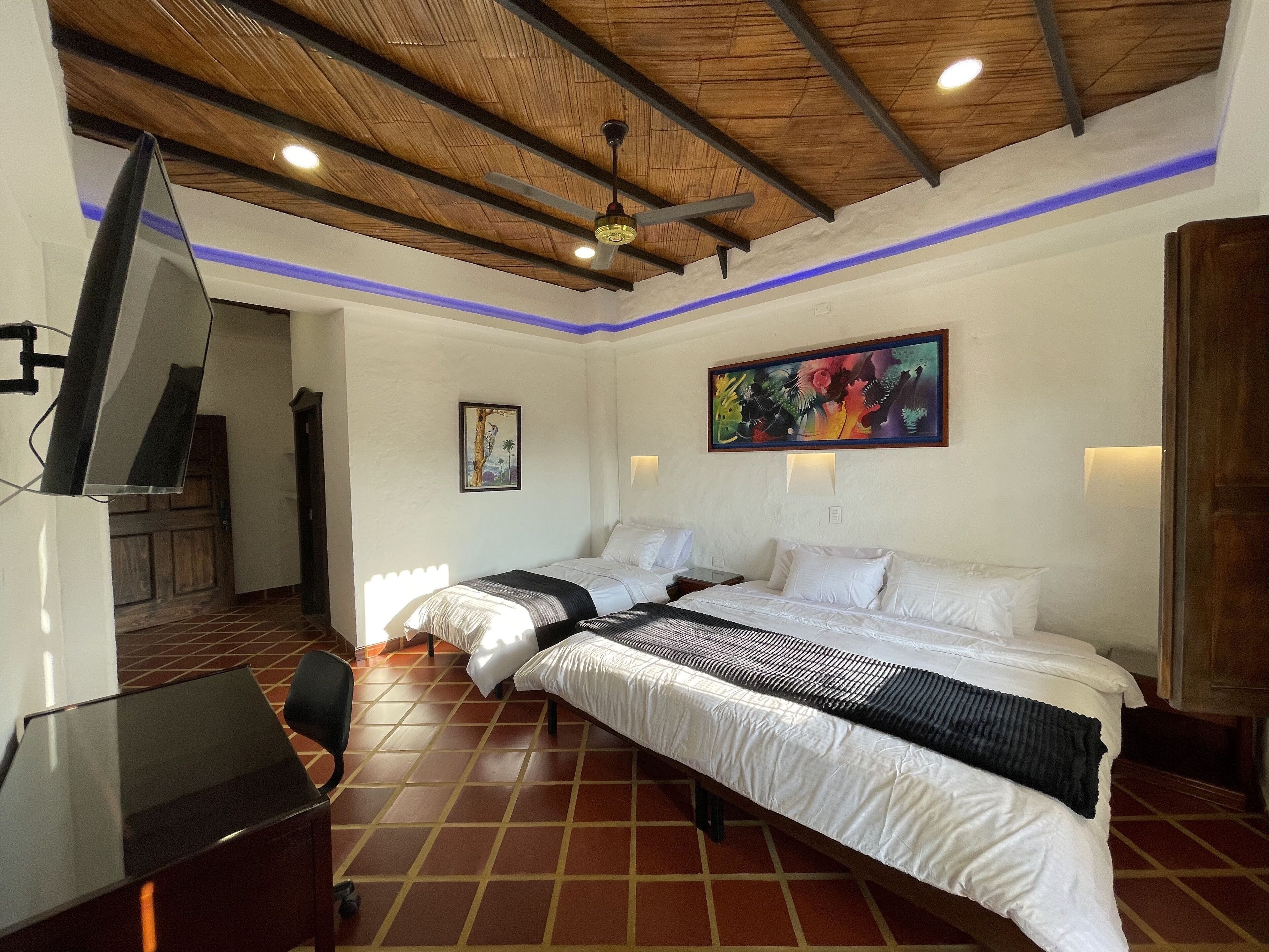 A hotel room with two beds, a desk, a TV, and a ceiling fan.