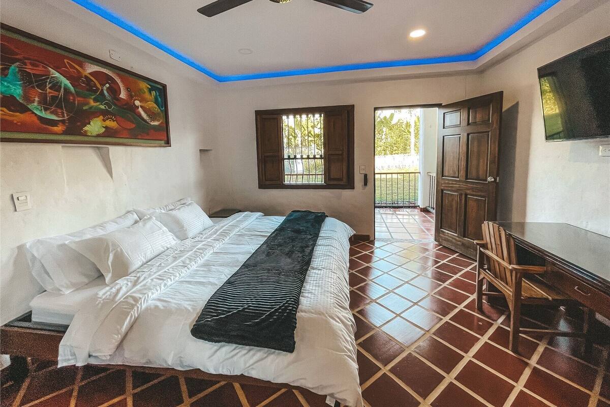 Une chambre à coucher avec un lit, un ventilateur de plafond, une fenêtre, une porte et un téléviseur fixé au mur.