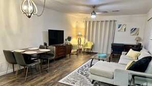 A modern living room with a dining area, a ceiling fan, a flat-screen TV, and a sofa. - Close to everything!  2bed/2 bath (Surprise)