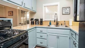 Une cuisine avec des meubles de couleur bleu clair, une cuisinière noire, un évier et une fenêtre avec des stores.