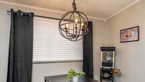 Un coin repas avec une table, des rideaux noirs, un luminaire suspendu, une petite plante et un appareil à pop-corn.