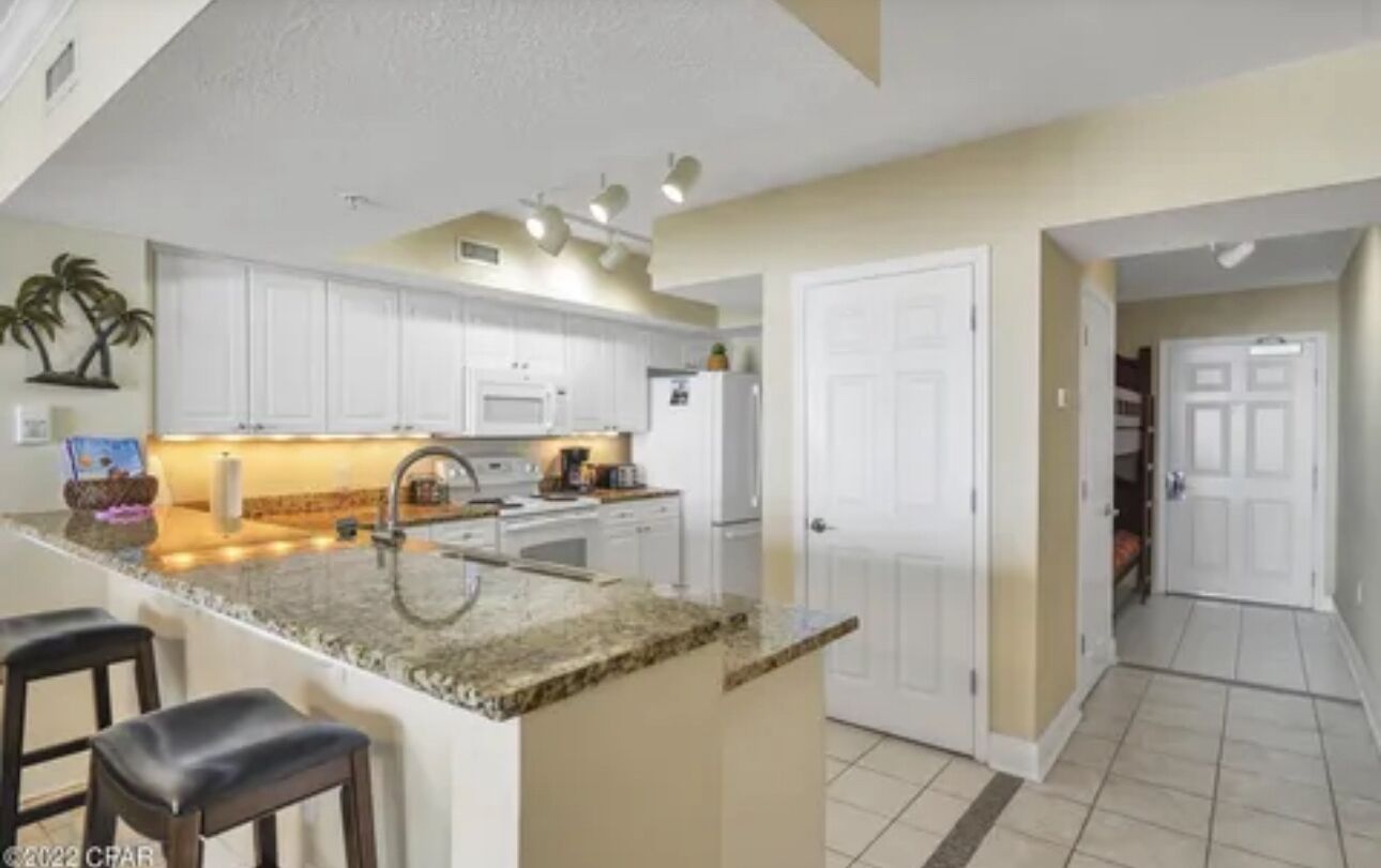 A kitchen with white cabinets, a granite countertop, and a central island with bar stools.
