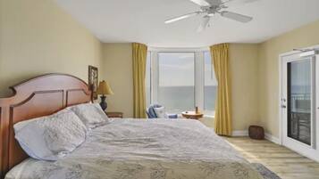 A bedroom with a bed, a ceiling fan, a window with curtains, and a view of the ocean.