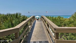 A wooden boardwalk leading to a beach area with a covered seating area and flags. - Gulf Front Condo in PCB, FL.
2 bedroom 2 bath with one set of bunks (Panama City Beach)