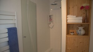 A bathroom with a glass shower enclosure, a wooden shelf with towels and a vase, and a blue towel hanging on a rack. - Idyllic Country Location for couples, central, peaceful, 5 mins from shops, WIFI (LOPEREC)